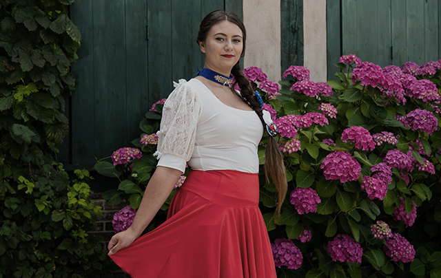 Femme en jupe rouge et top blanc, posant avec assurance pour une photo, mettant en valeur son style et sa personnalité